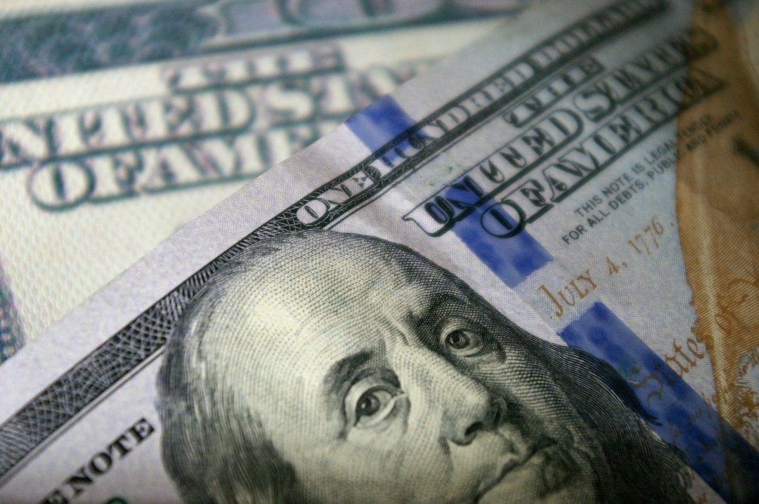 US dollar bills beside a stock-market screen